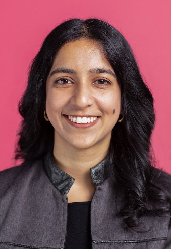 An indian woman smiling in front of a pink background.